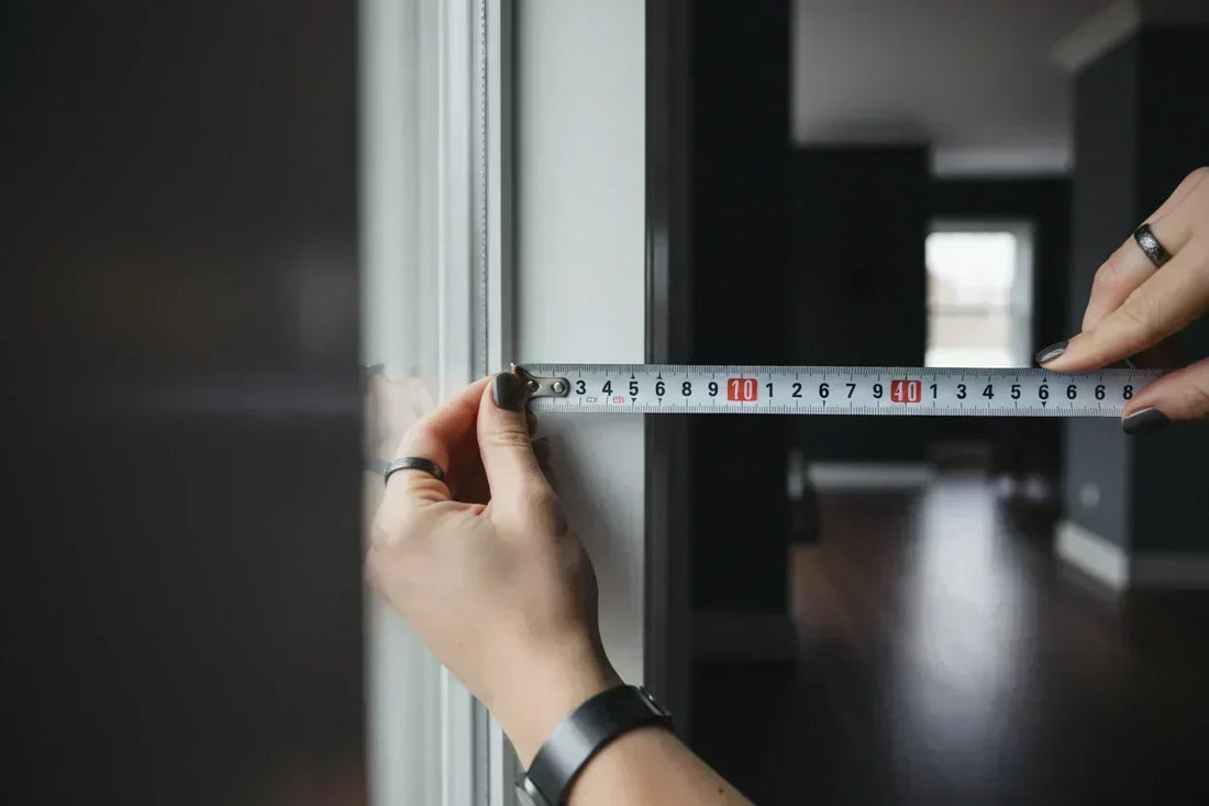 Hands using a steel tape measure to measure a window frame for cellular shades installation