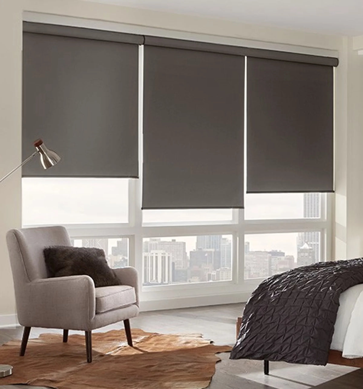 Three cordless dark charcoal blackout roller shades covering large bedroom windows with city skyline view
