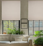 Dual cordless white blackout roller shades on black-framed windows in a modern brick wall living room with plants
