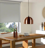 Cordless wipe-clean roller shade beside a rustic dining room table with copper pendant lighting and outdoor view
