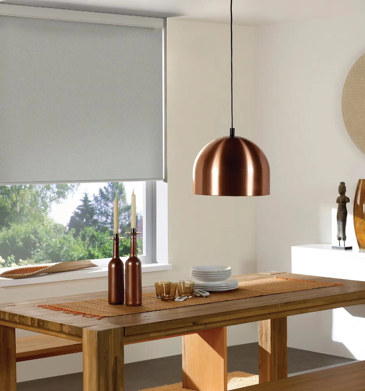 Cordless wipe-clean roller shade beside a rustic dining room table with copper pendant lighting and outdoor view
